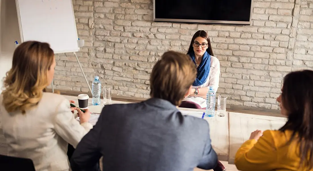 Young woman sitting facing three interviewers – two women and a man. She’s smiling because she got some great interview tips.