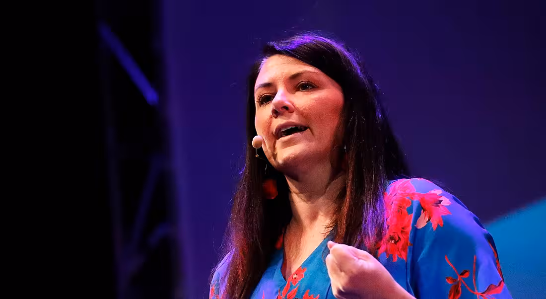 A close-up of a confident, dark-haired woman speaking at a conference about the future of work.