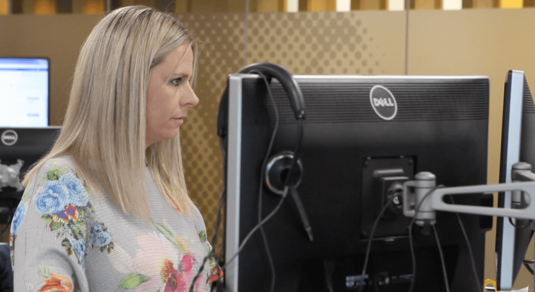 Blonde woman sitting at a computer concentrating on her duties as technical capabilities manager