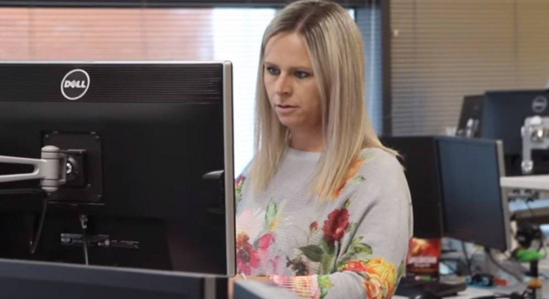 Blonde woman in a flowery jumper working at a computer in the Liberty IT offices.