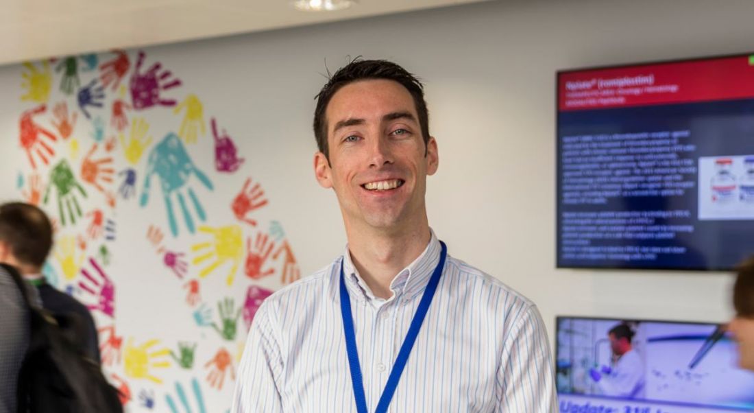 A young man in a powdery blue shirt grinning at the camera in Amgen.