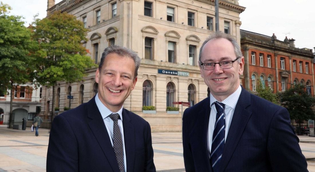 Two middle-aged men in suits looking directly into the camera and smiling widely against the backdrop of Danske Bank.