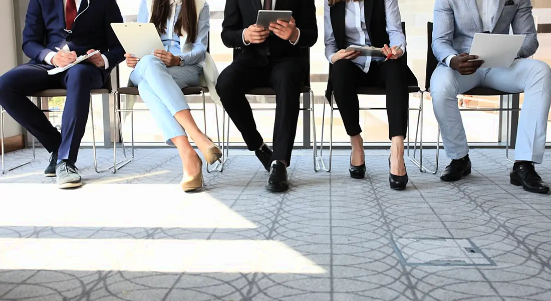 A group of young people sitting in a waiting room waiting to go into a job interview, part of tech recruitment process.