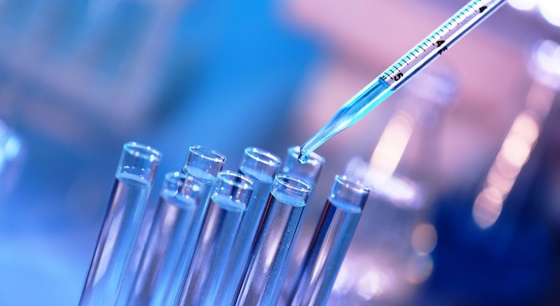 A close-up of blue liquid being dropped into a test tube using a pipette.