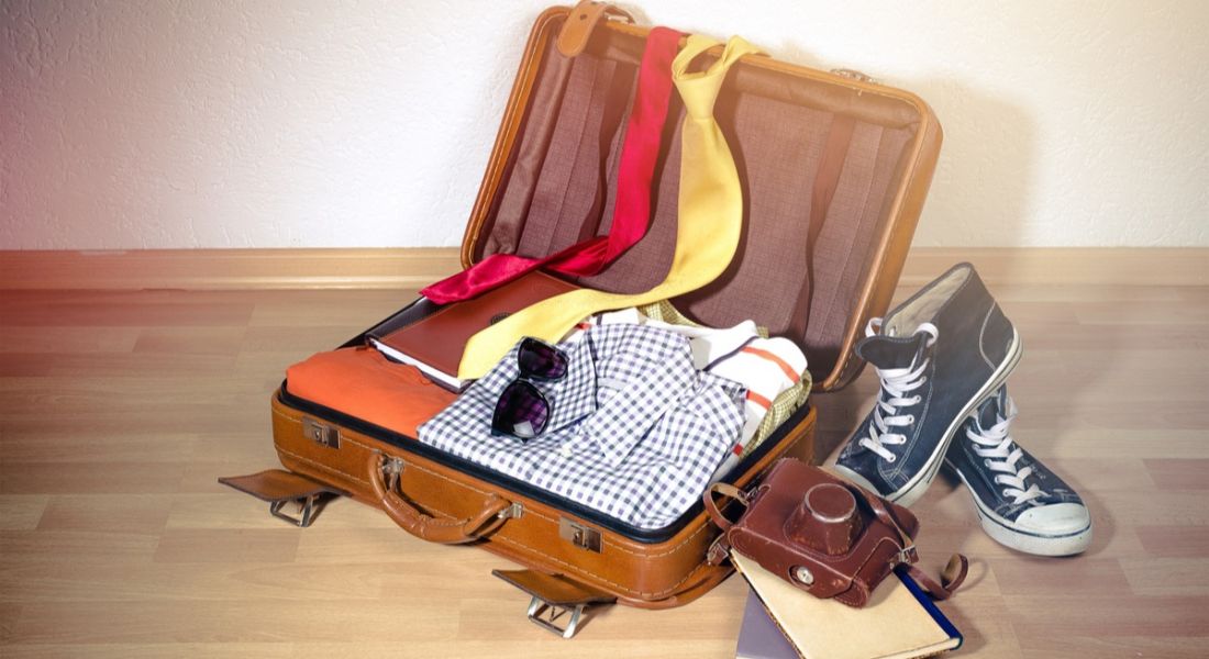 An open suitcase with shirts, ties and shoes strewn around it.