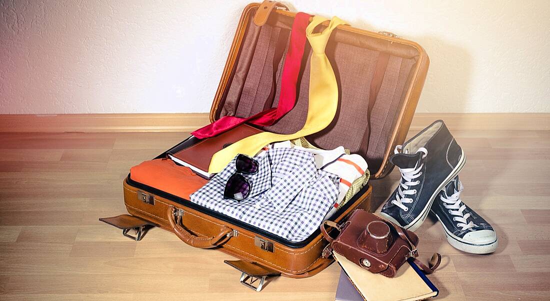 An open suitcase with shirts, ties and shoes strewn around it.