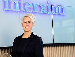 A man in a casual zip-top with Interxion written on it stands cross-armed, leaning against a glass wall.