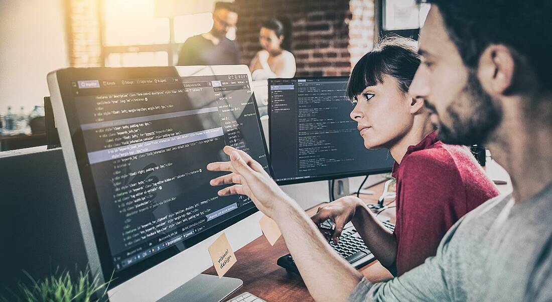 Man and woman looking at code on computer screen.