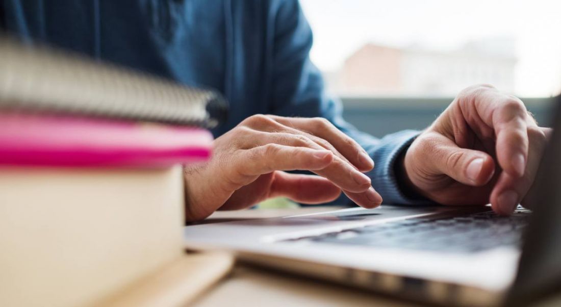 A view of the hjands of a software developer floating over a silver laptop with a stack of books in the foreground.