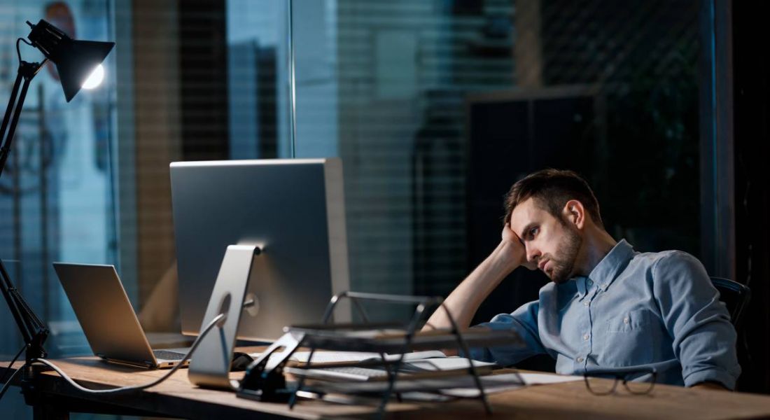 Casual man looking fatigue while working with computer in dark office alone.