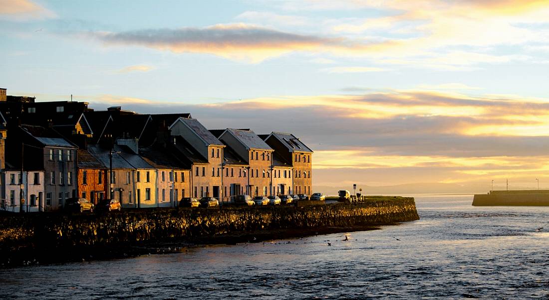 A blue and yellow sunrise peeling over a waterfront dotted with old painted homes.