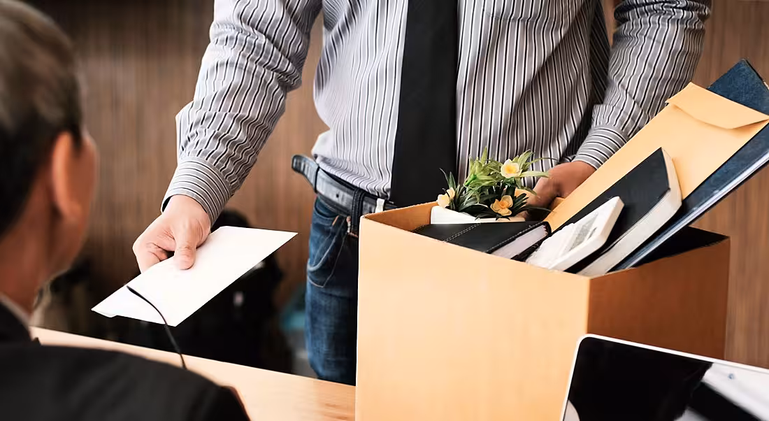 Shot of torso of business man handing in resignation letter to boss with his box of stuff in hand.