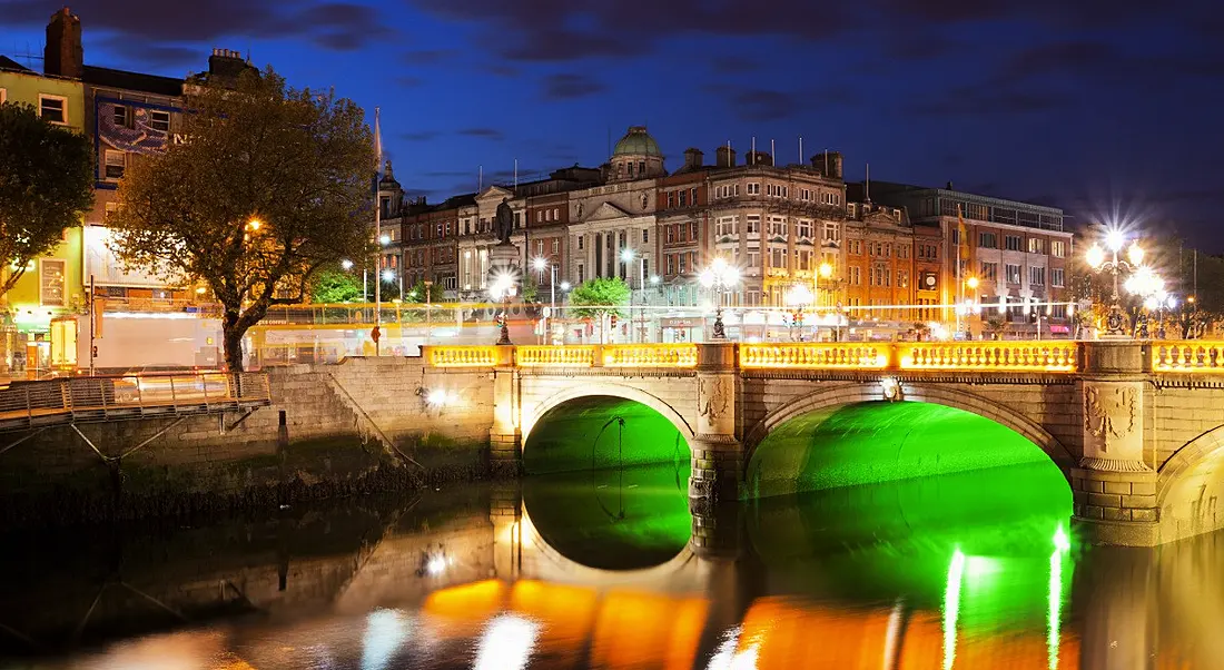 A river veining through the city of Dublin illuminated at night with green and orange lights. Dublin’s iconic Georgian style architecture can be seen.