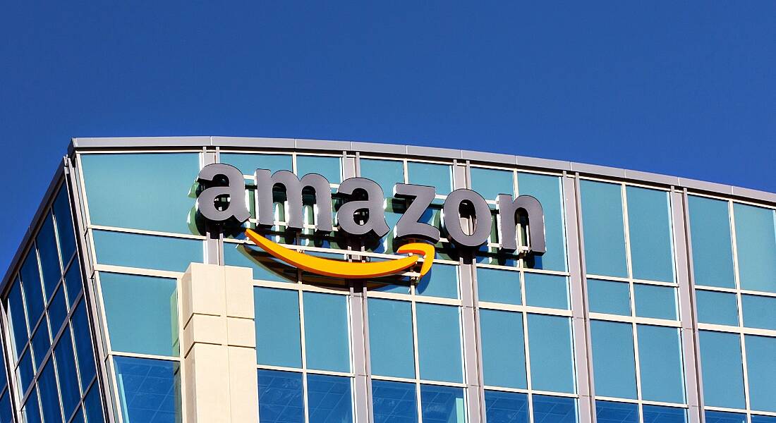 An image of the Amazon company logo on a glass building on a sunny, clear morning in Santa Clara, California.