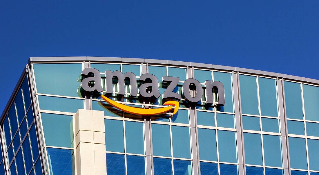 An image of the Amazon company logo on a glass building on a sunny, clear morning in Santa Clara, California.