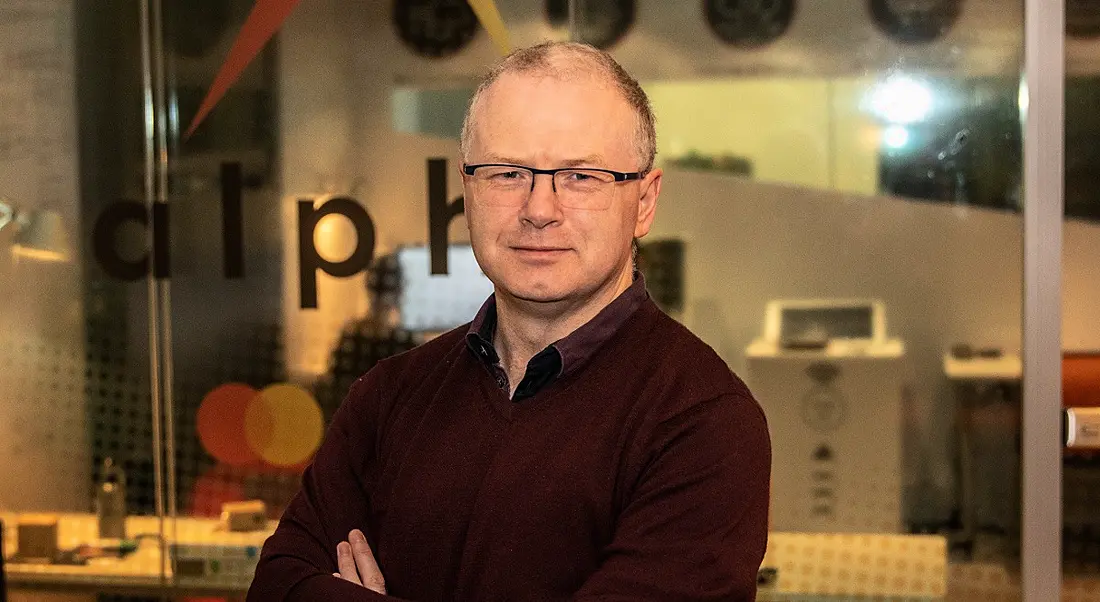 A headshot of a middle-aged man in Mastercard with fair hair and folded arms wearing glasses and a red jumper over a shirt.