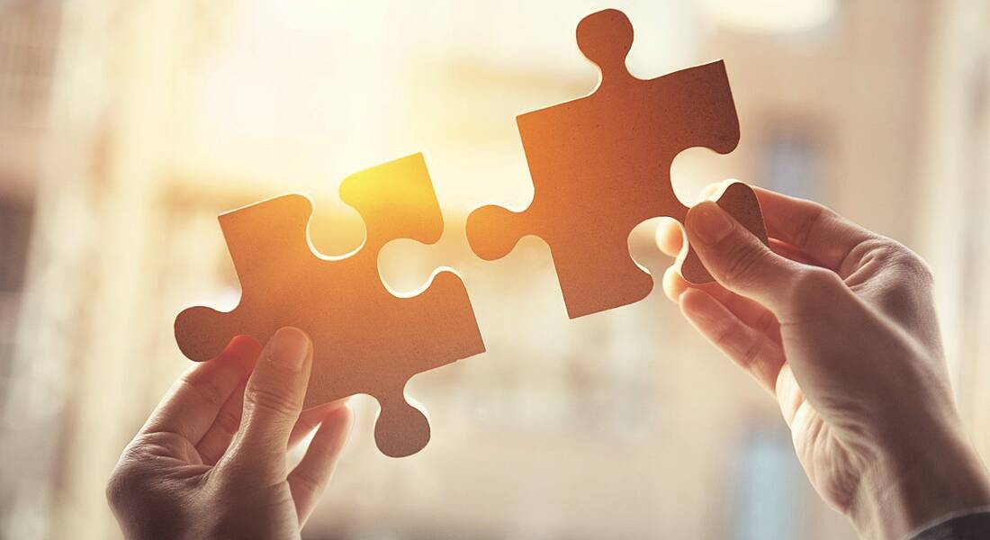 Two hands holding up two large jigsaw pieces against orange sunlight, representing company culture fit.
