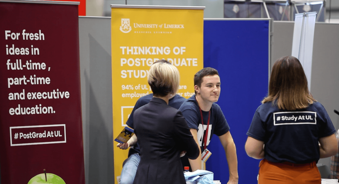 A few people in UL t-shirts in front of colourful banners at the UL Careers Fair.