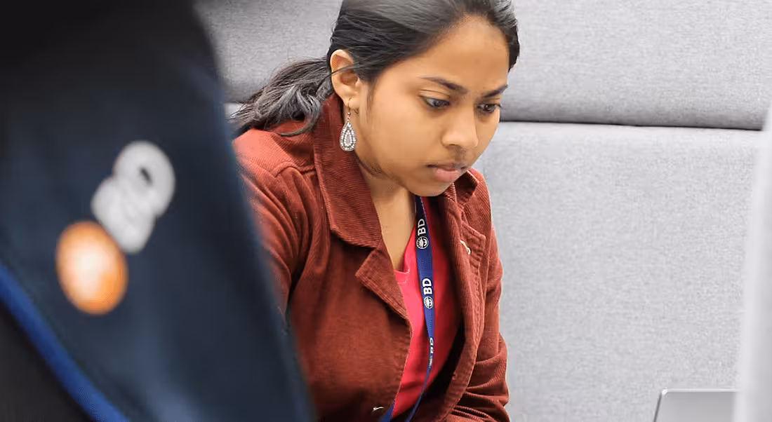 A young woman with her hair pulled back in a low ponytail working at BD and staring intently at her laptop.