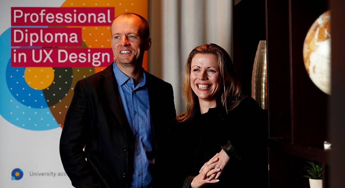 A ginger haired man and blonde woman smiling while looking off to the side at a UX Design Institute launch