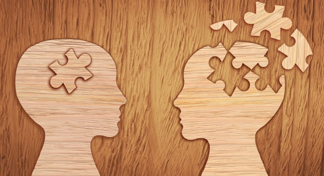 A wooden surface with two wooden heads facing each other. One has broken jigsaw pieces showing poor mental health.