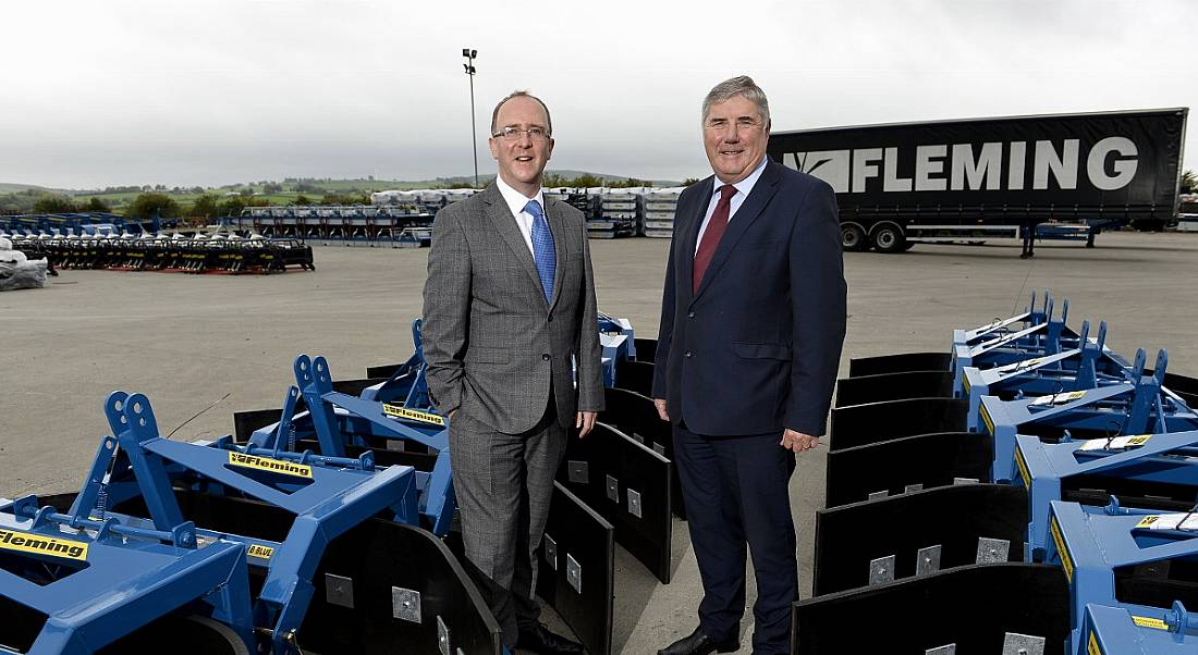 Two suited men smiling and standing among ground-level machinery manufactured by Fleming Agri.