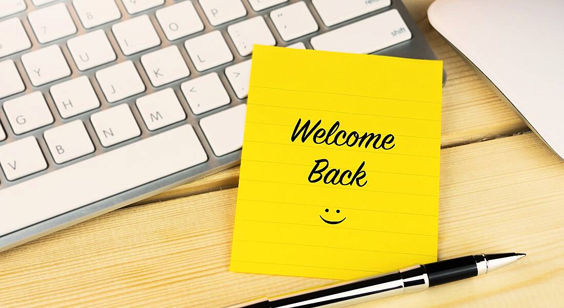 A yellow sticky note on a keyboard reads ‘Welcome Back’ with a smiley face.