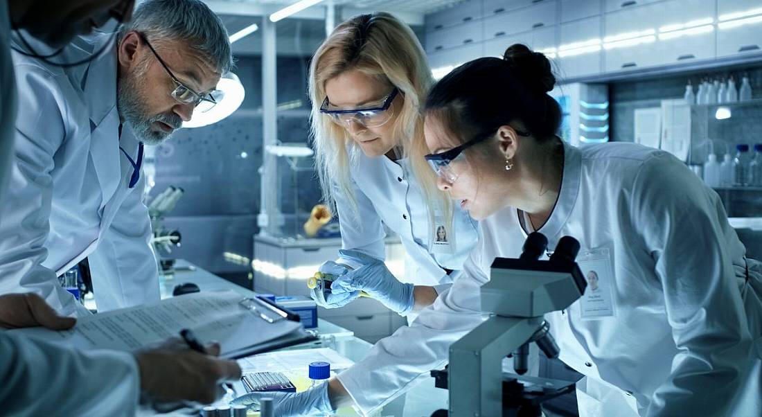 A group of scientists in labcoats huddled over equipment.