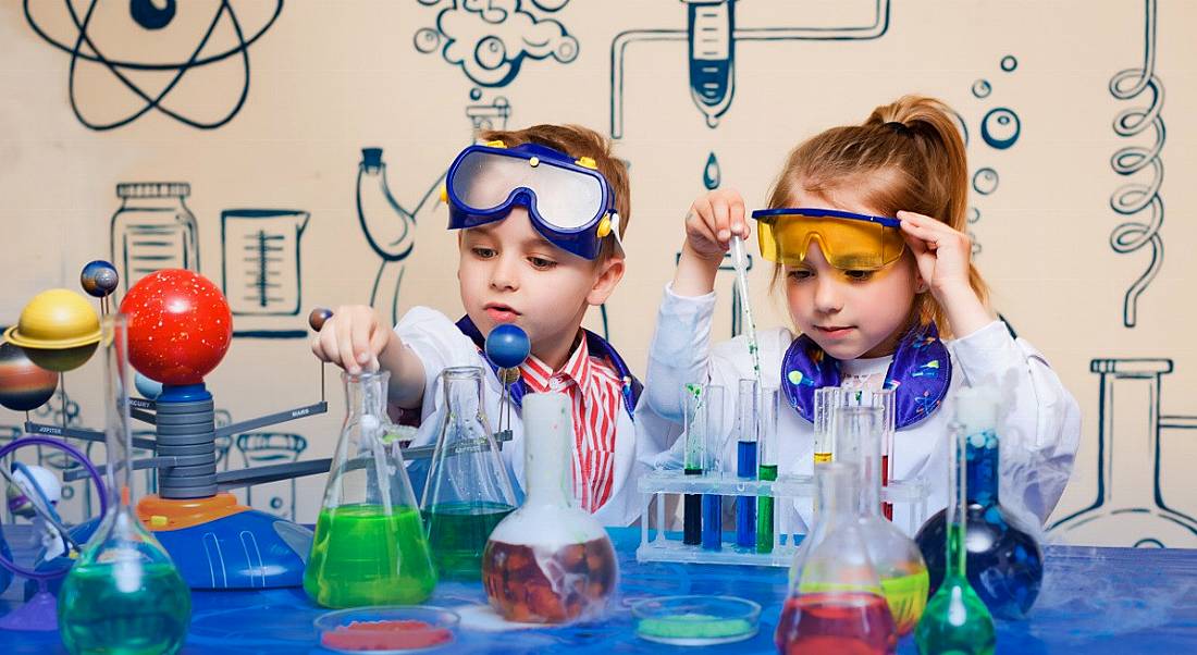 A young boy and girl dressed as scientists, playing with an assortment of beakers, dreaming of a science career.