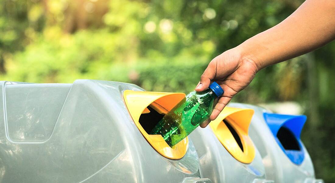 View of a hand placing a plastic bottle into a recycling bin on a sunny day.