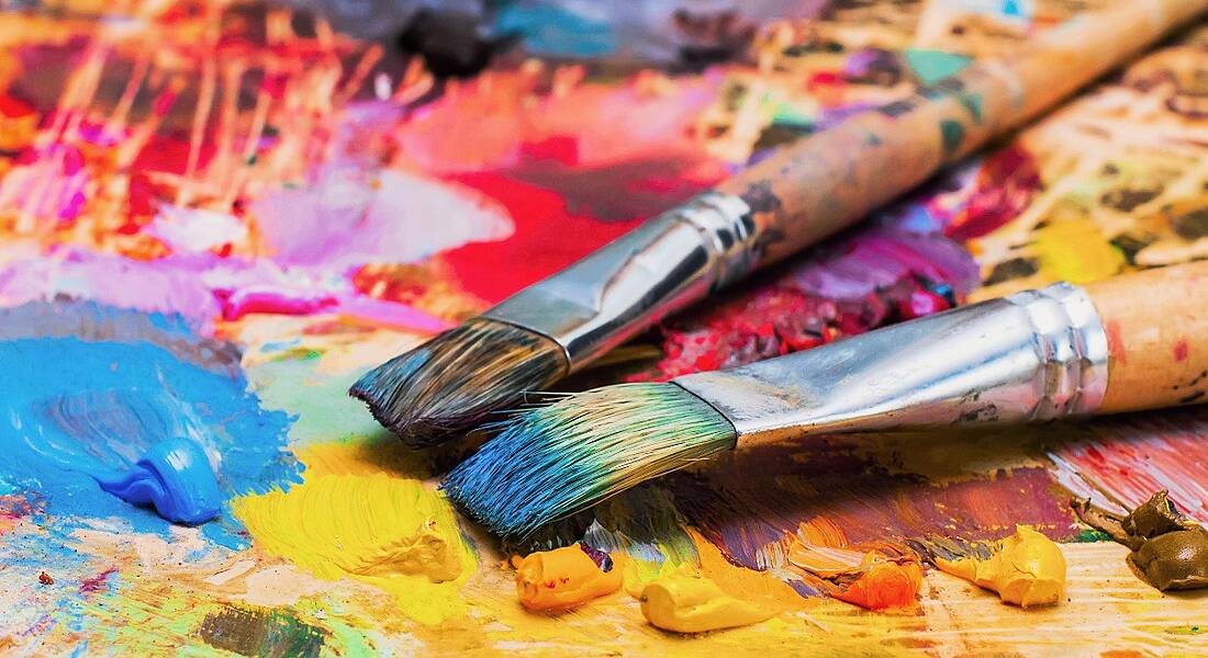 Used brushes on an artist's palette of colourful oil paint for drawing and painting.