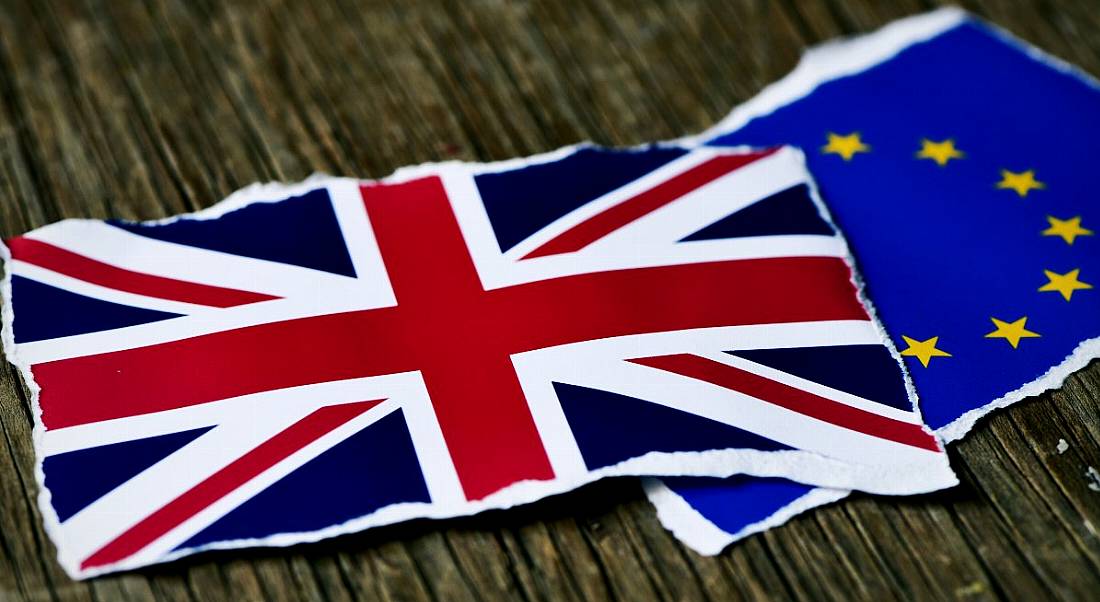 Two torn pieces of paper, one showing the UK flag, the other showing the EU flag on a wooden table, representing Brexit.