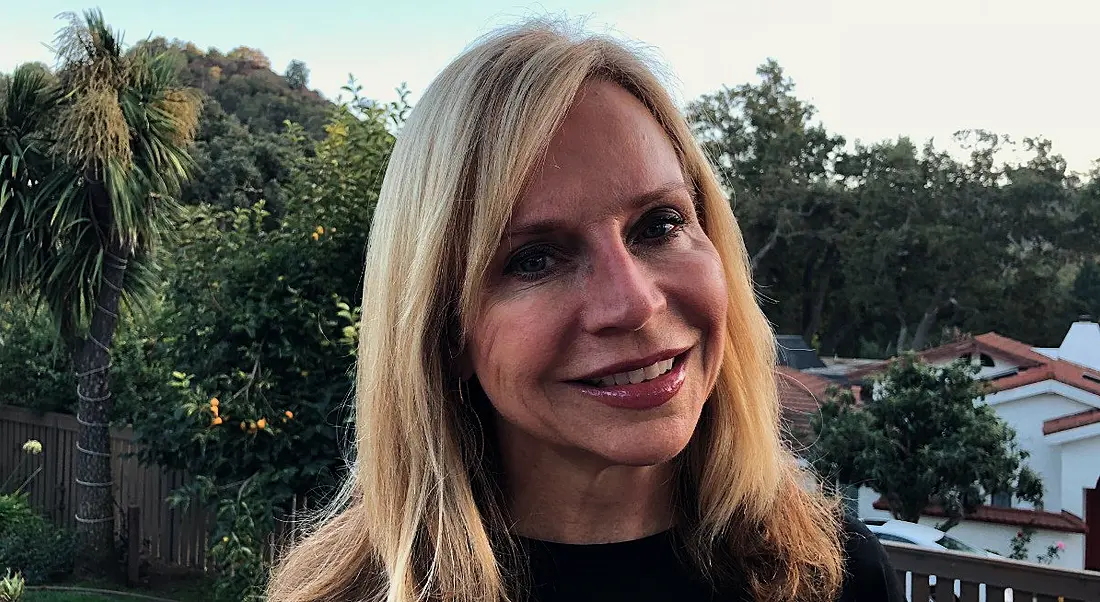 A blonde smiling woman against a scenic outdoor background. She is the CHRO of Symantec.