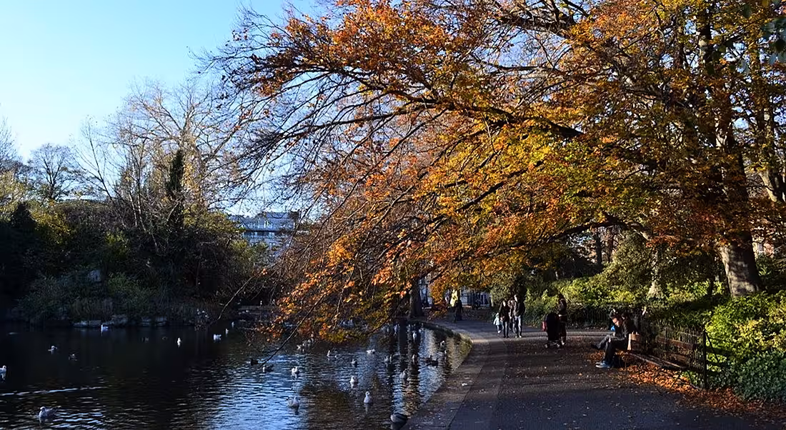People walking alongside lake in St Stephen's Green Dublin on an autumn afternoon.