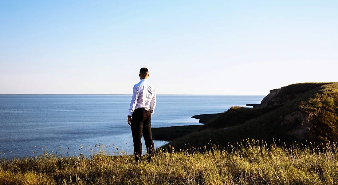 A man stands on the edge of a cliff looking out at the sea, pondering the future of work and the possible jobs.