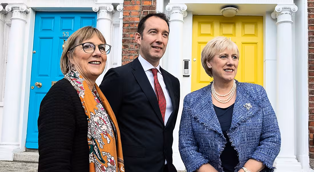 Close up woman and two men looking off into the distance on a blustery Dublin street with a bright yellow door in the background.