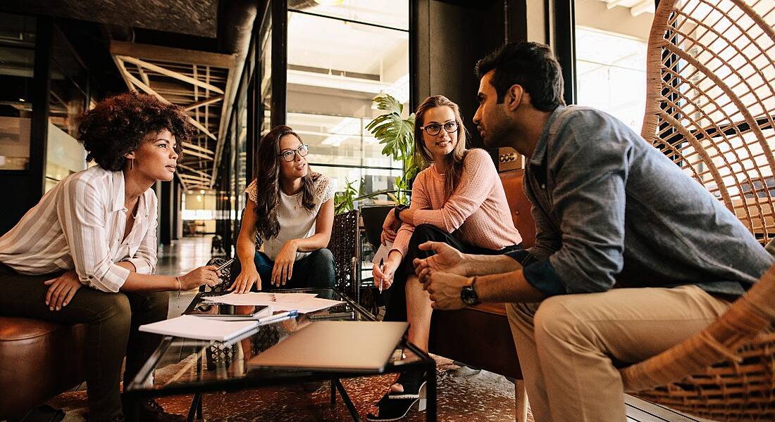 A diverse group of millennials sitting around in a comfortable room collaborating together.