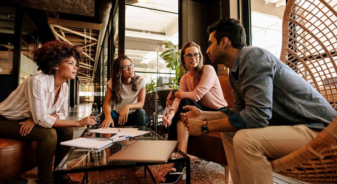 A diverse group of millennials sitting around in a comfortable room collaborating together.