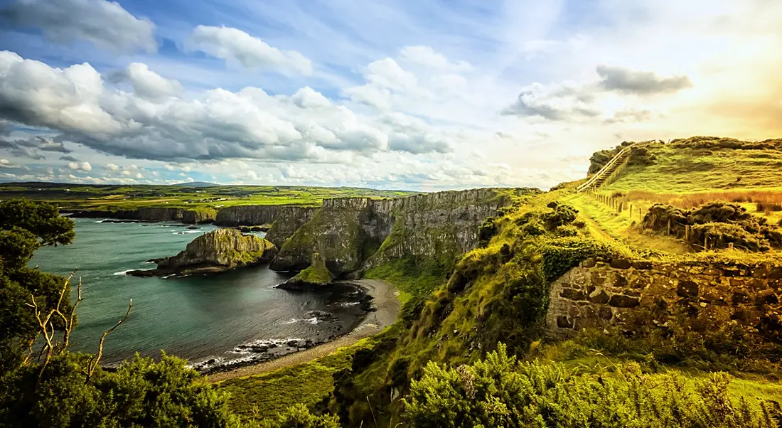 A view of the coast of northern ireland with the sunrise streaming over the rolling hills.