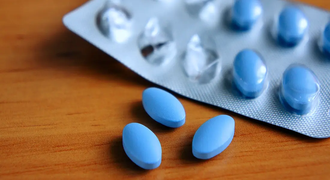 Image of blue pills spilling out of a blister packet on an oak wood table.