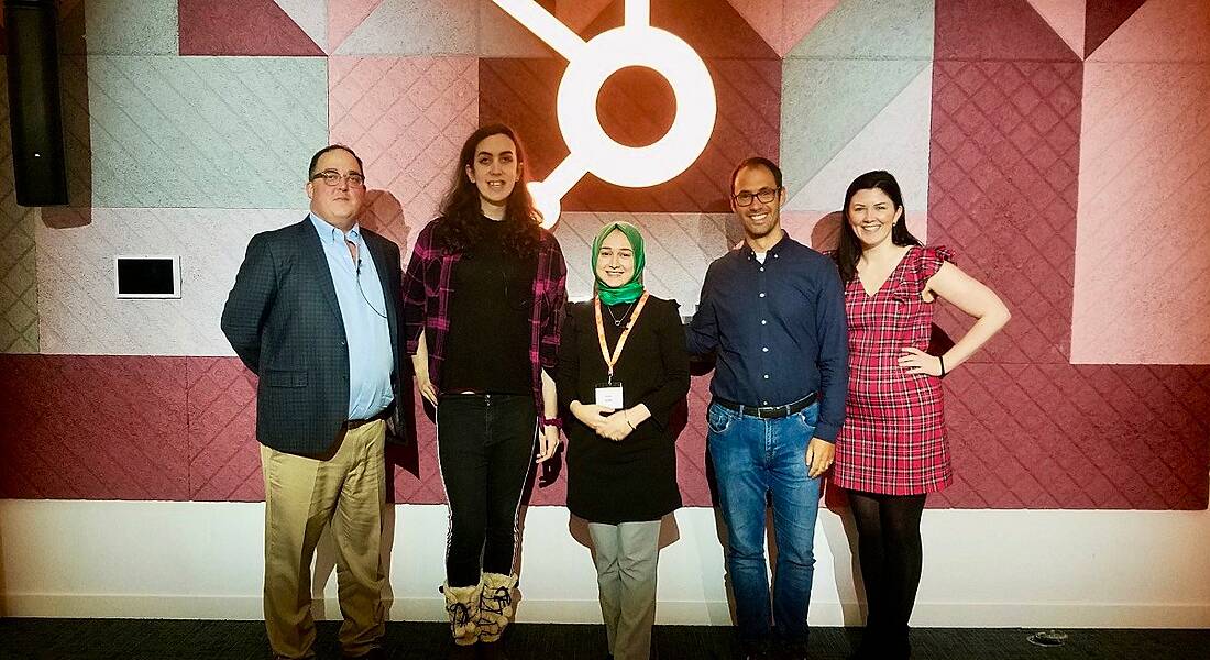 Five diverse people stand in a row smiling in front of the HubSpot logo following a diversity and inclusion event.