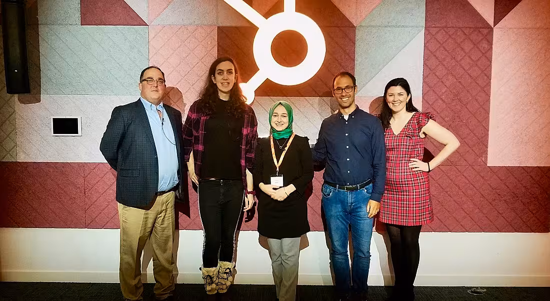 Five diverse people stand in a row smiling in front of the HubSpot logo following a diversity and inclusion event.