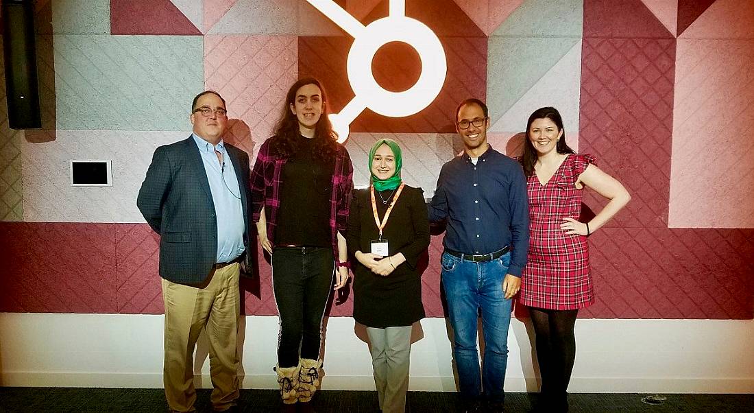 Five diverse people stand in a row smiling in front of the HubSpot logo following a diversity and inclusion event.