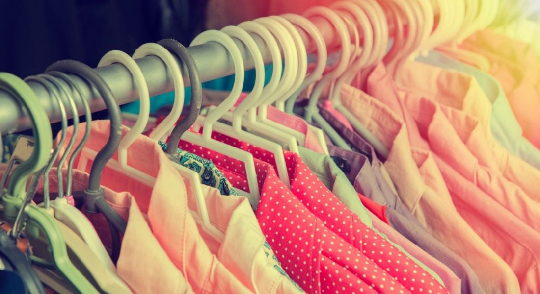 A close-up of a rail full of different coloured clothes with a sun ray coming from the top right corner.