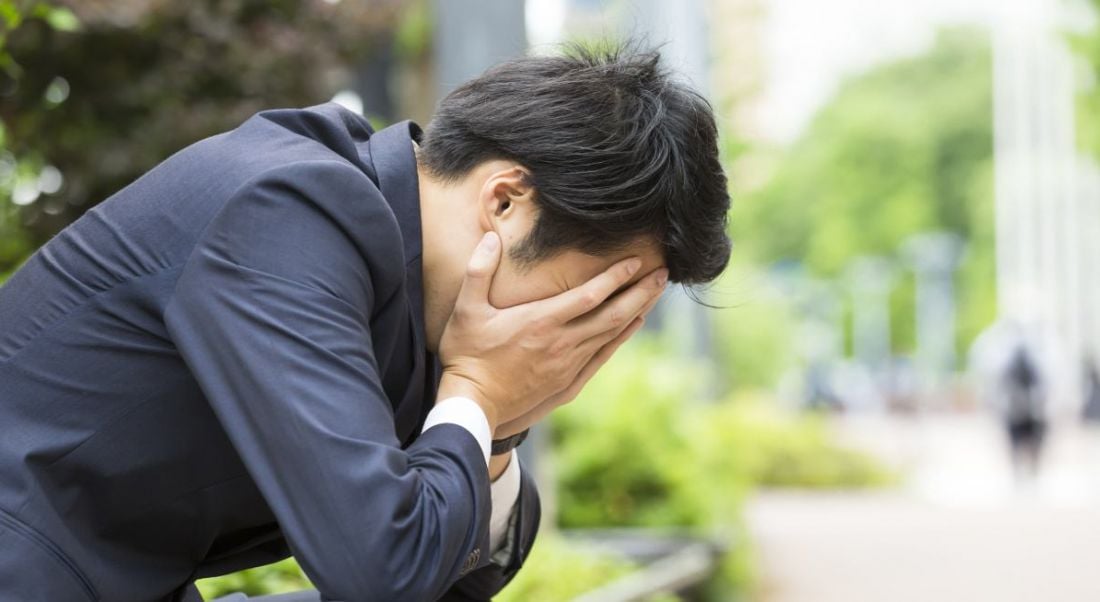 A man in a business suit sitting on a bench outside with his head in his hands. He just had a bad job interview.