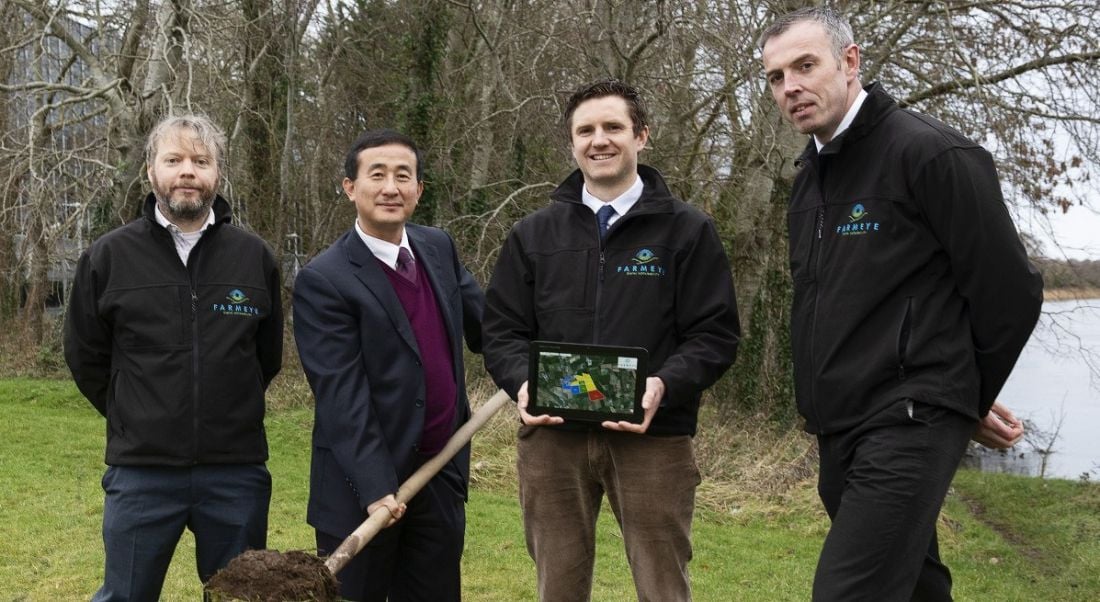 Four men in a field with one holding a shovel of soil.