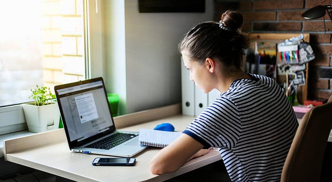 A girl sitting at a desk working on a laptop. She’s concentrating and learning the art of self-discipline.