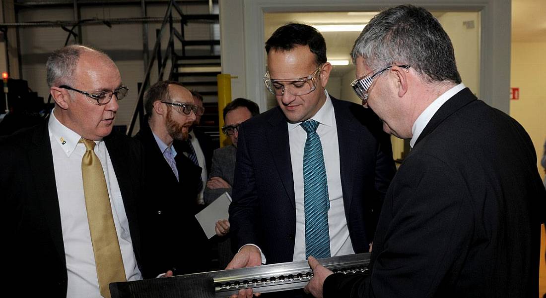 Three suited men looking down at and inspecting a long, thin titanium aircraft part.