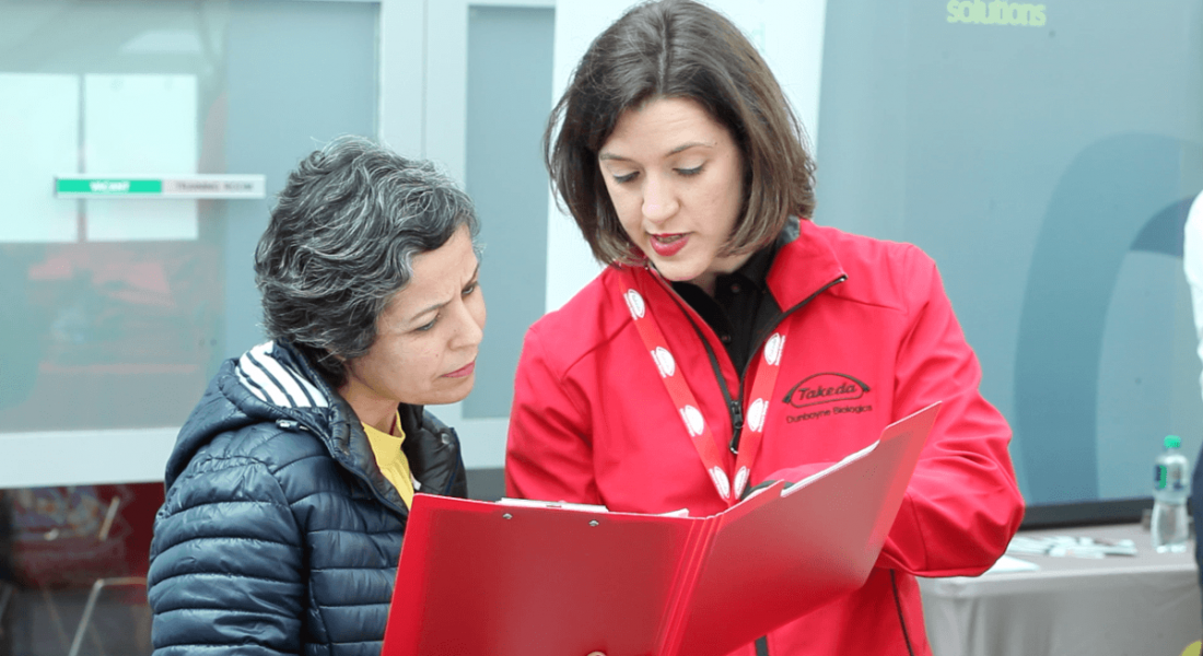A woman in a red Takeda jacket at the NIBRT Careers in Biopharma event talking to another woman about opportunities.