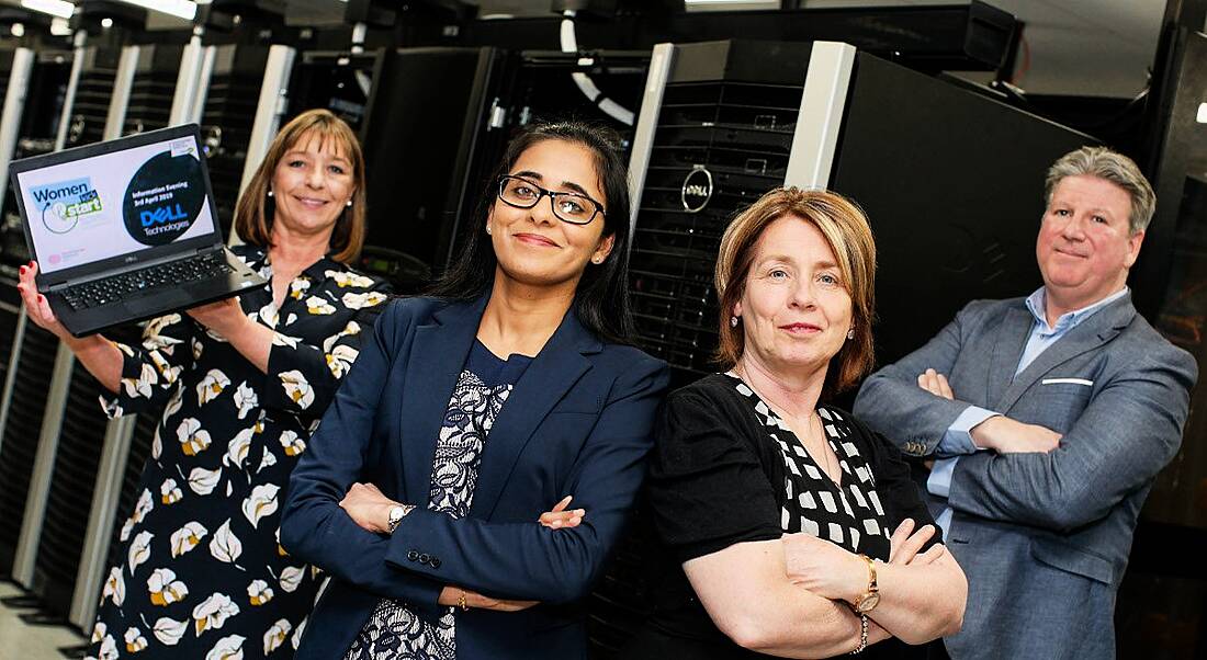 Three women and a man standing in a server room.